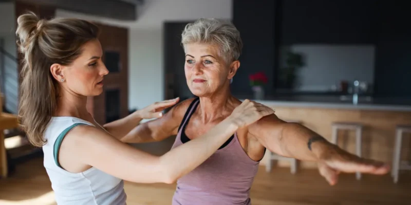Personal trainer helping an older woman with a balance exercise at home