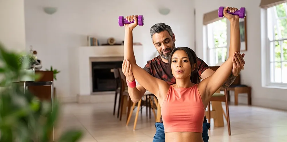 Personal trainer coaching a client with dumbbells during an in-home session