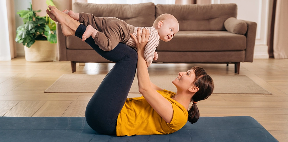 New mother doing a postpartum workout at home on a mat, lifting her baby